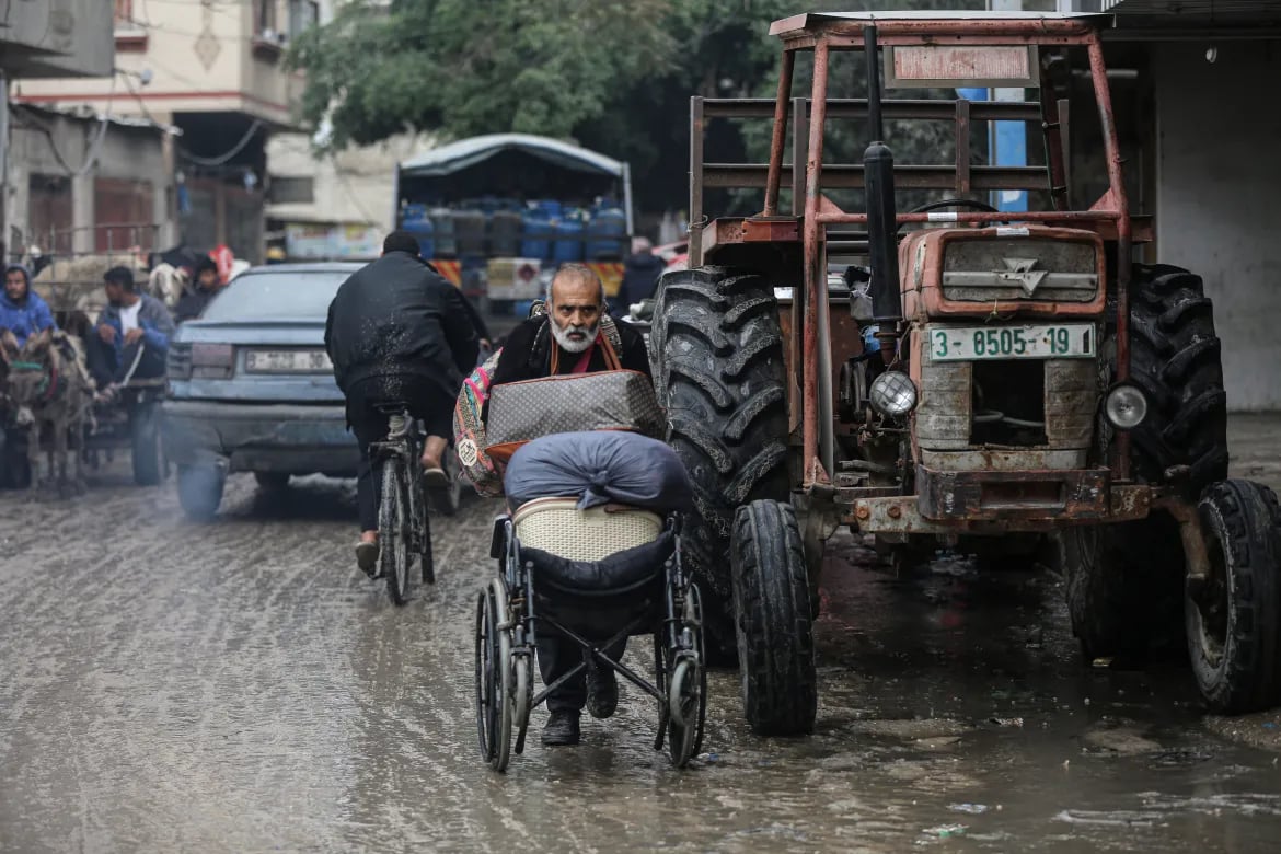Displaced Palestinians push belongings in a wheelchair through waterlogged Nuseirat streets.