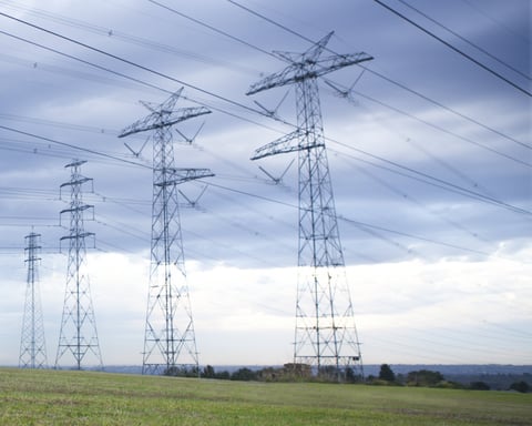 High-voltage power transmission lines against a blue sky representing the challenge of managing complex renewable energy grids